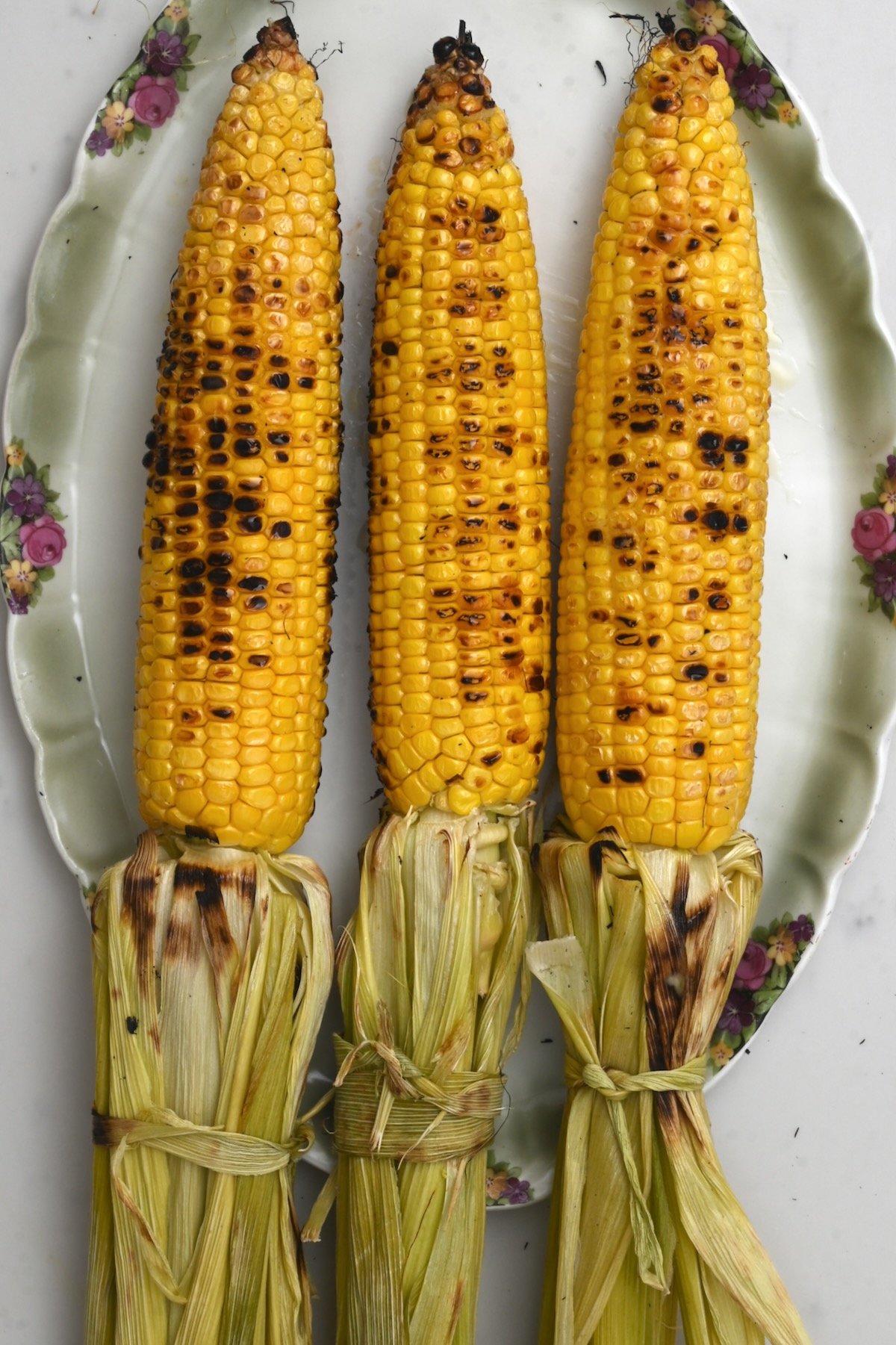 three grilled corn on the cob with the husk tied to the back on a green plate