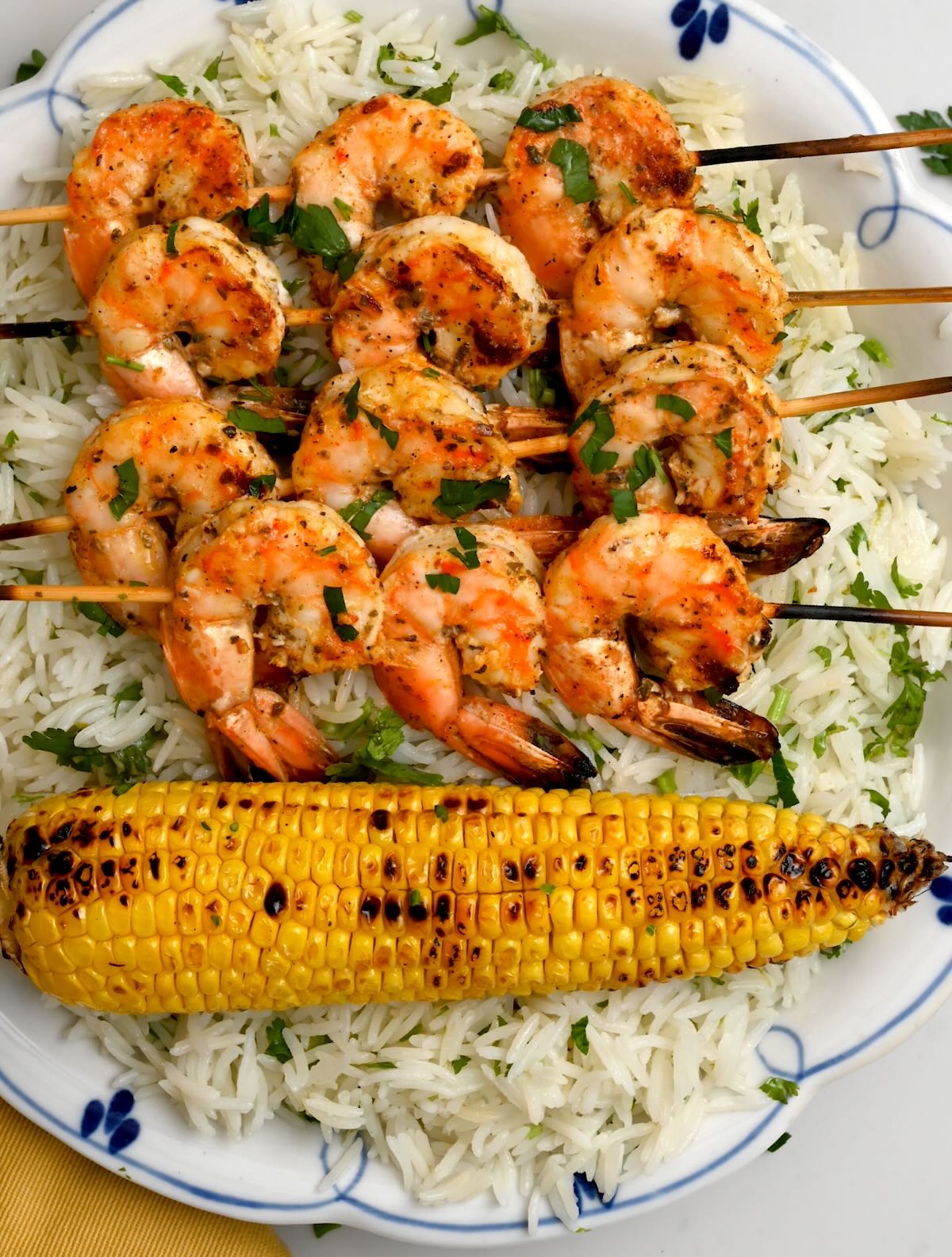 grilled corn on the cob served with grilled shrimp skewers on top of rice