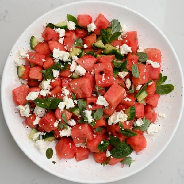 Top view of watermelon feta salad in a white large bowl on a white marble background.