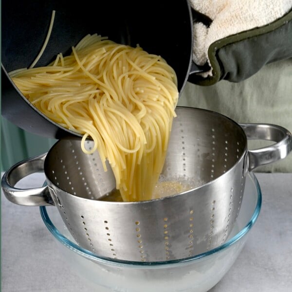 Square photo of pouring cooked spaghetti into a colander over a glass jar