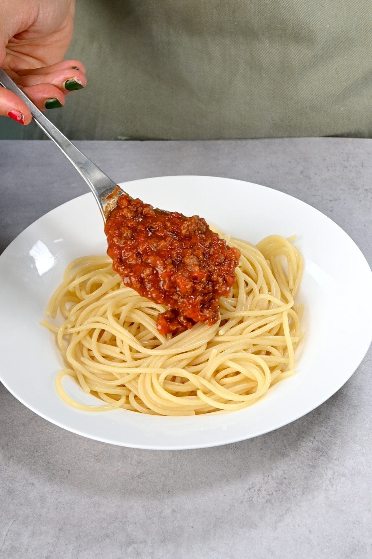 Close-up side view of pouring meat sauce over cooked spaghetti on a white plate.