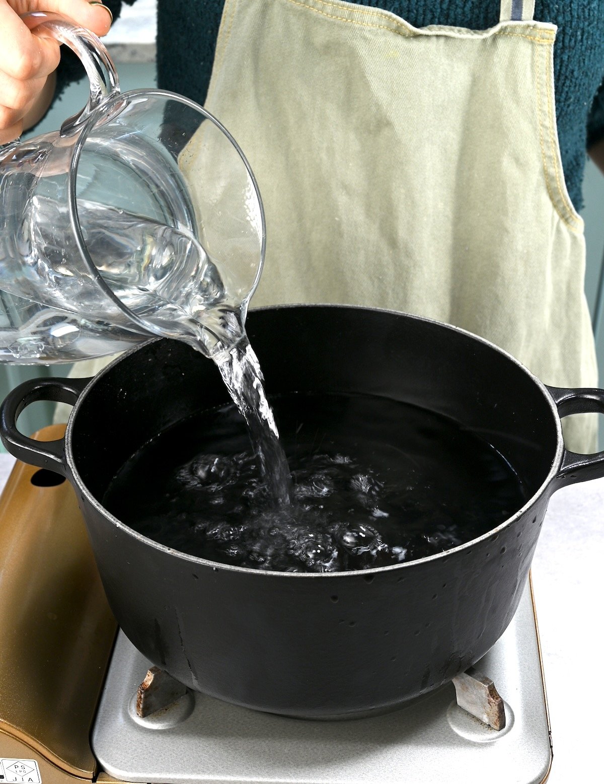 Side view of pouring water from a glass jar into a black pot.