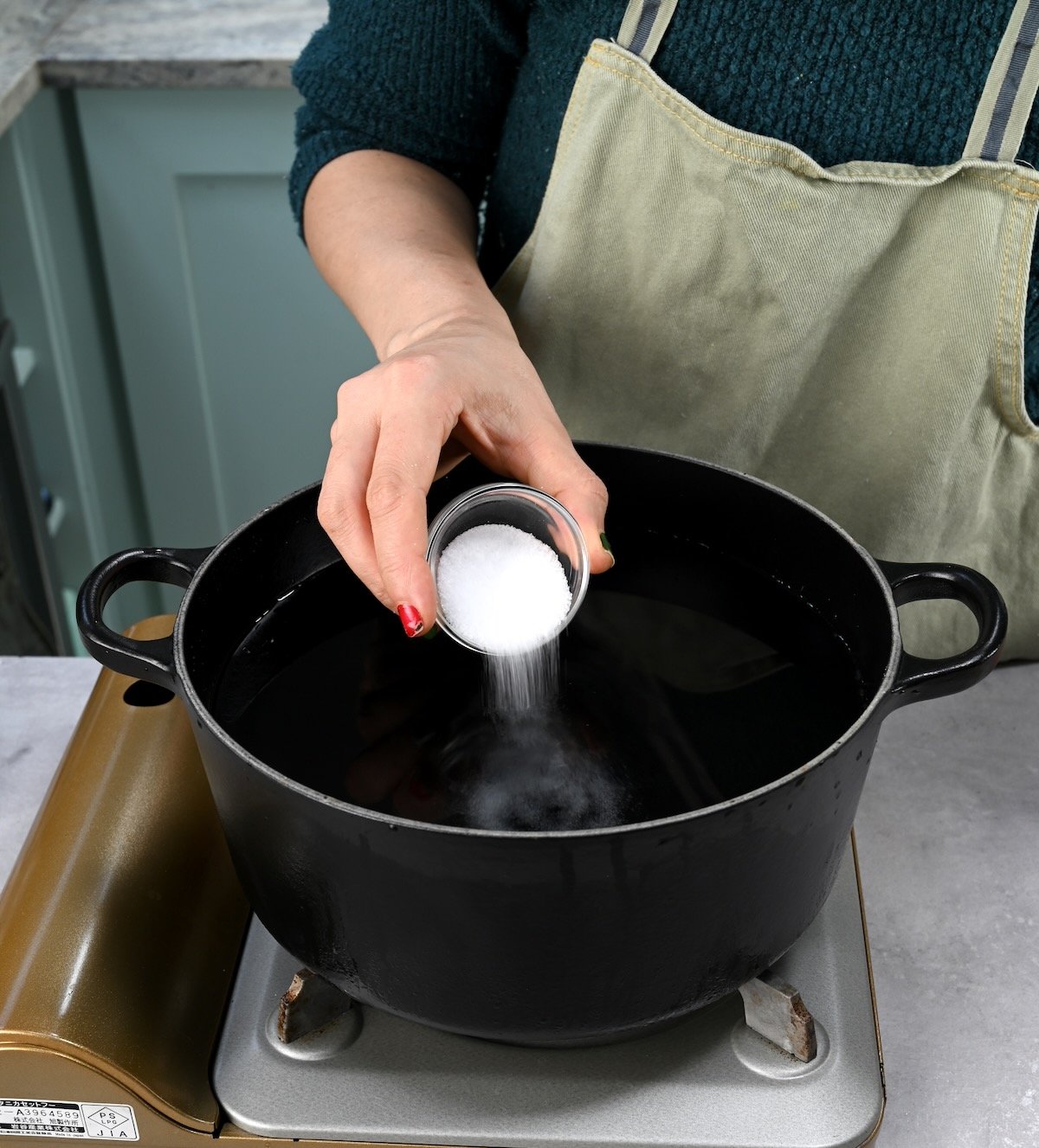 Side view of me adding salt to a black pot filled with water.