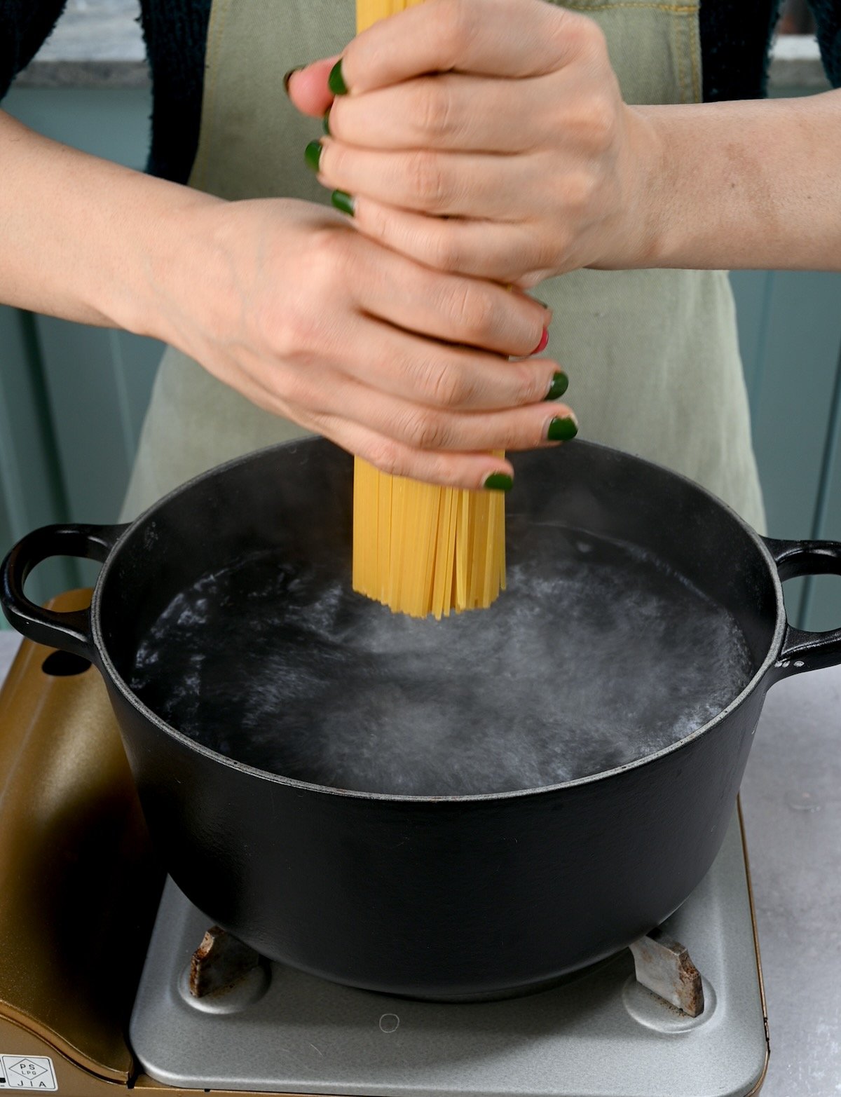 Side view of me placing dry spaghetti into a pot of boiling water.