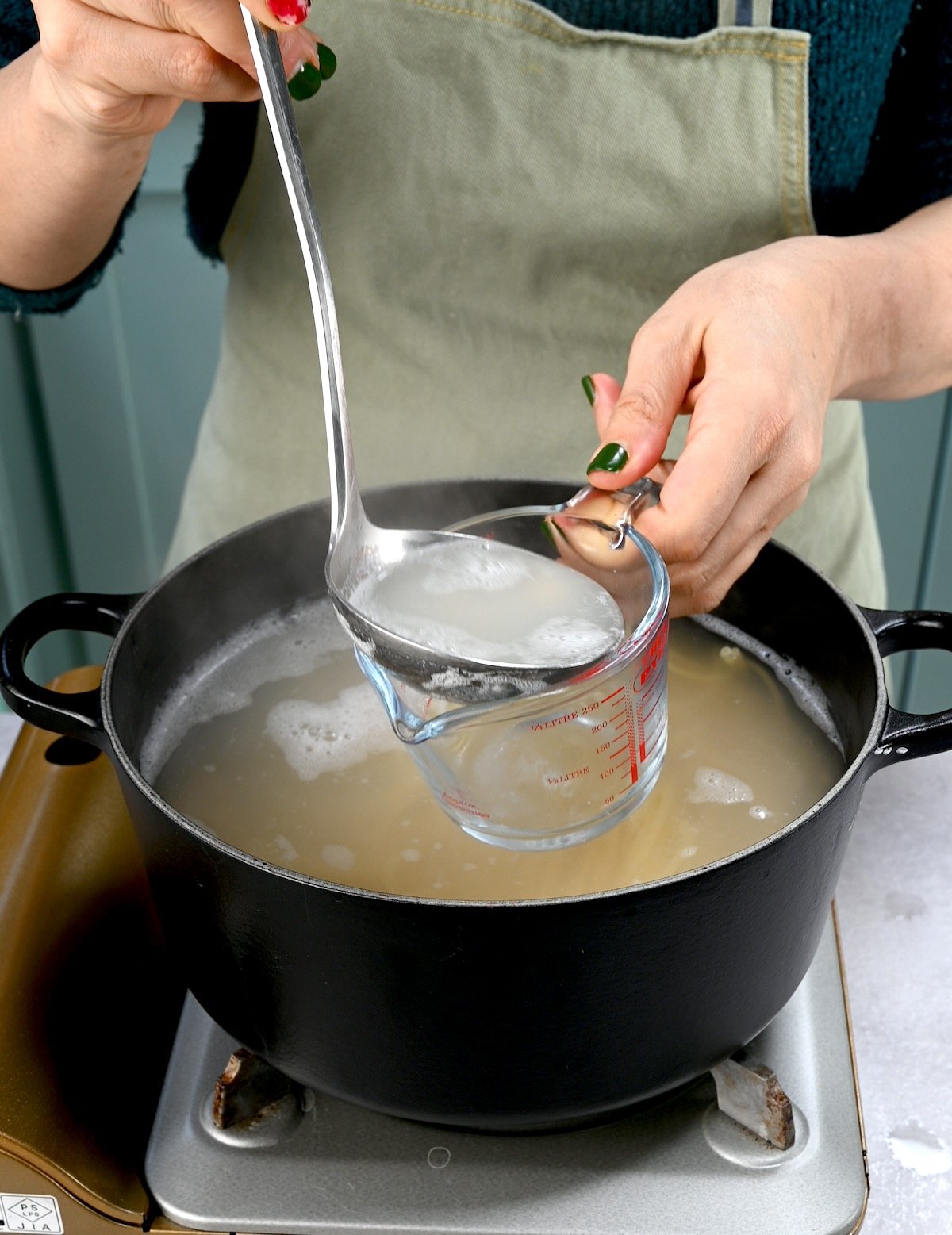 Side view of a ladle pouring reserved pasta water into a clear cup.