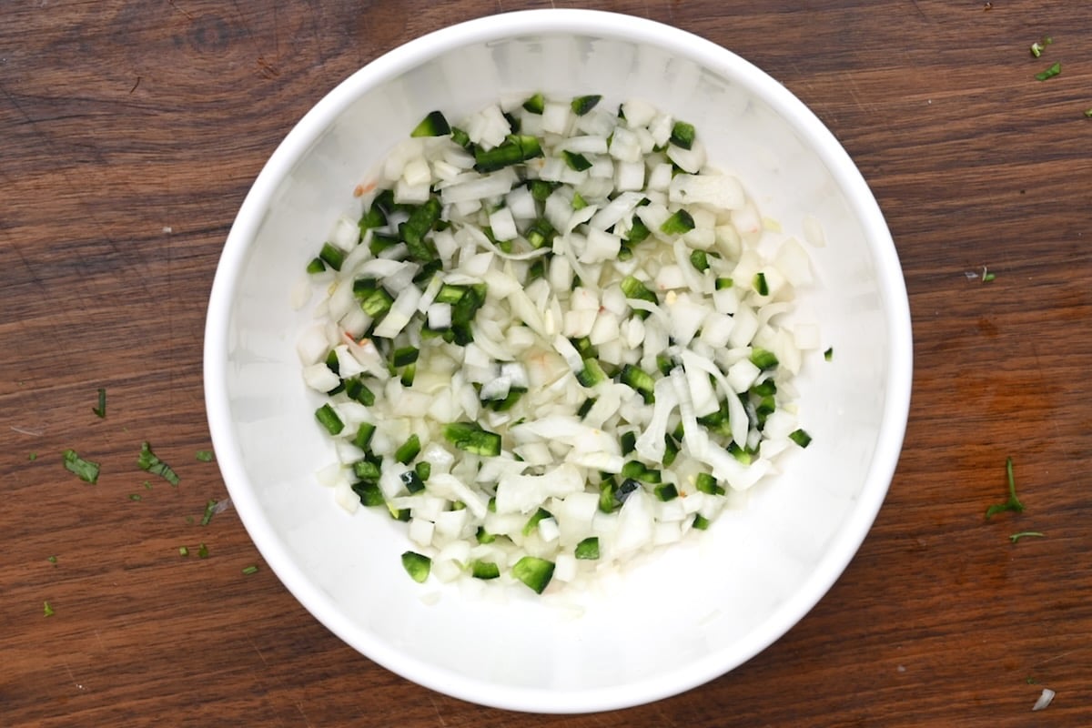 Top view of sliced white onion, jalapeño, and lime juice soaking in a white bowl on a wooden surface. - 13