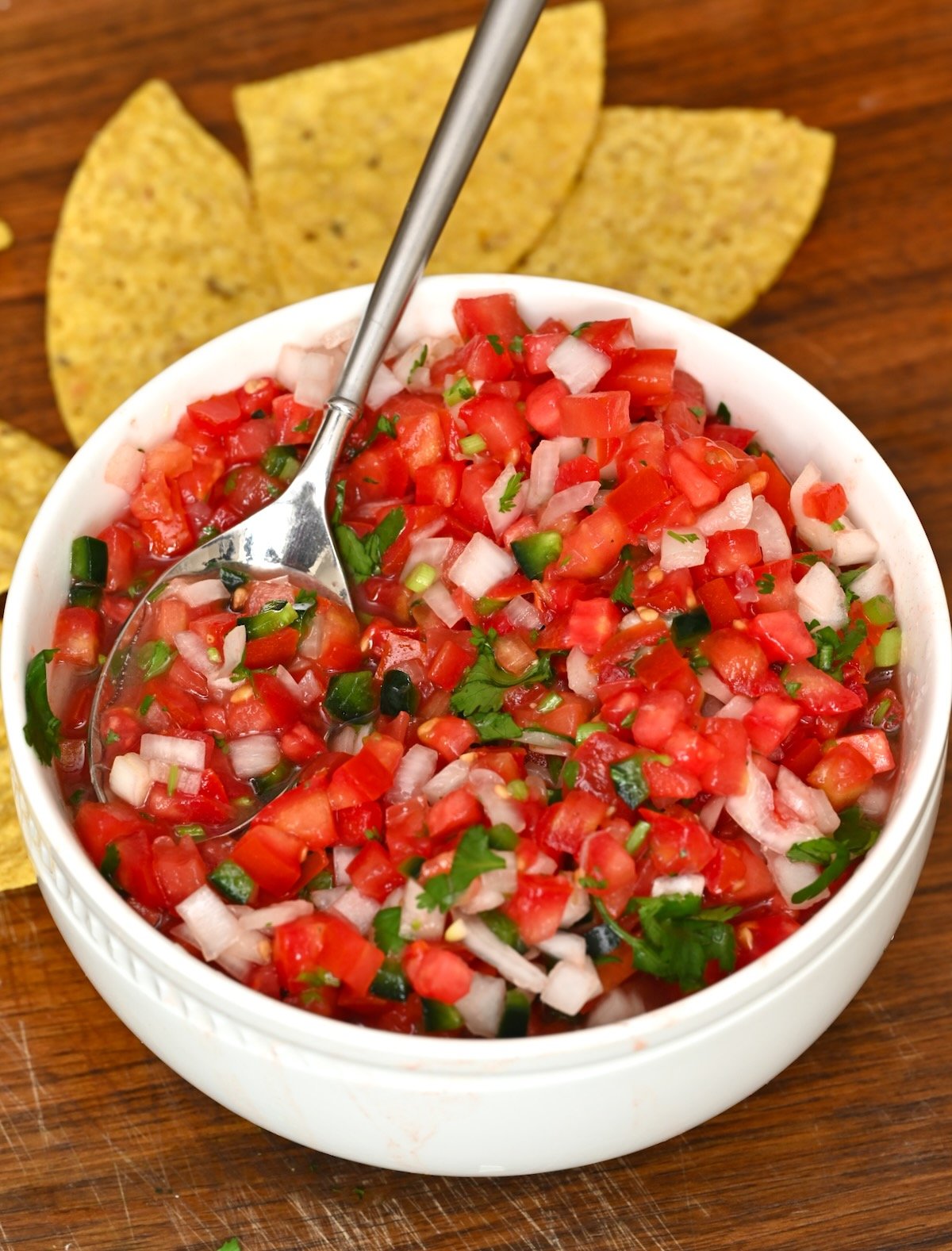 Side view close-up of a bowl of pico de gallo with a spoonful lifted and tortilla chips in the background. - 10