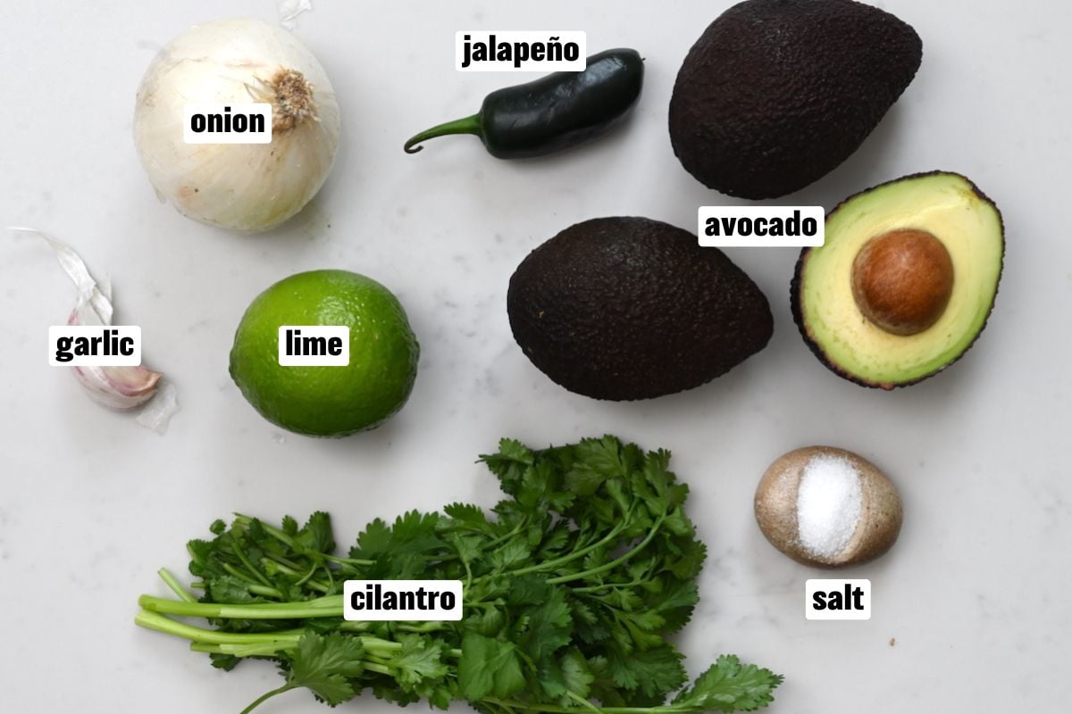 top view of the ingredients for making guacamole recipe on white marble.