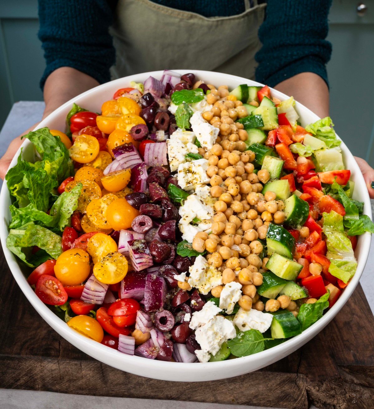Side view of a large bowl of Mediterranean salad being held by hand.