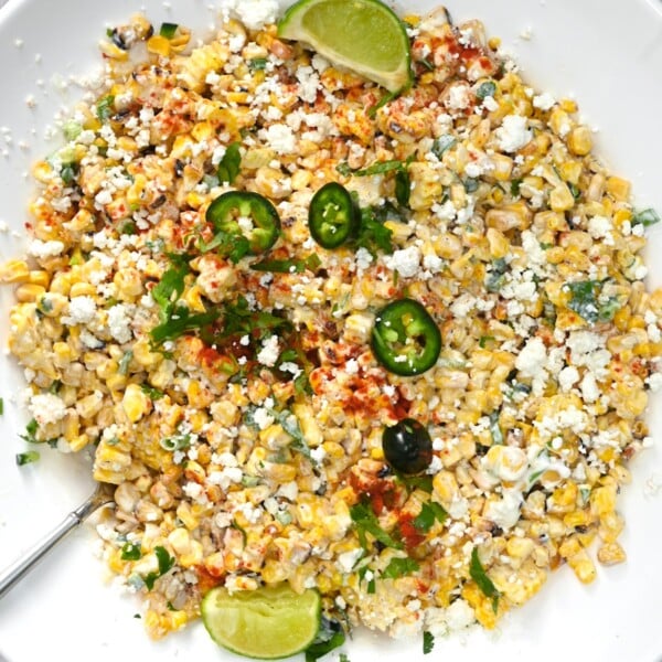 top view close up of mexican street corn salad in a white plate garnished with some lime wedges and jalapenos