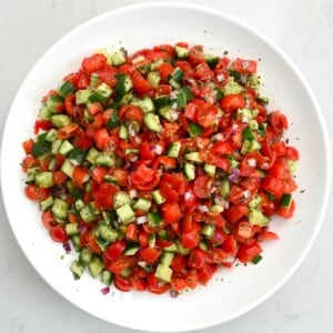 top view of shirazi salad in a white large plate on white marble background.