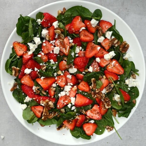 Top view of strawberry spinach salad in a white bowl on a grey background.