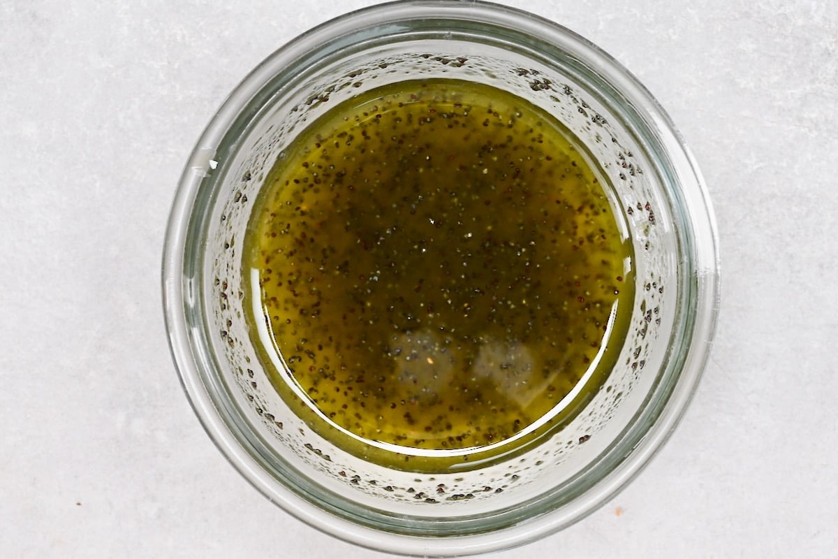 Overhead shot of a glass jar filled with strawberry spinach salad dressing, with visible poppy seeds.