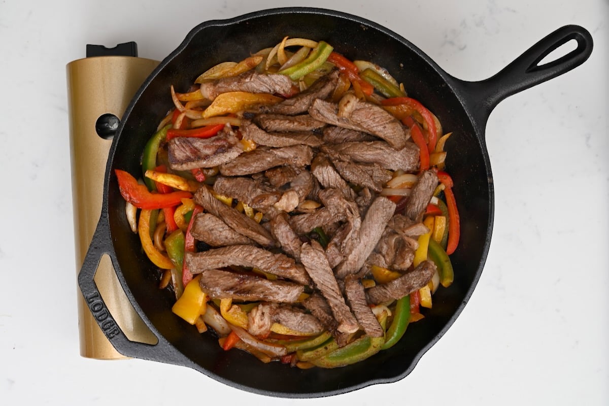 steak sliced and placed on top of cooked peppers in a black cast iron skillet
