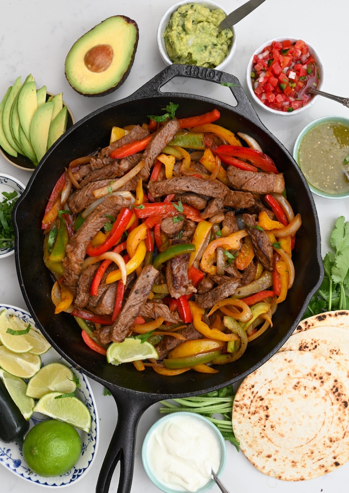 top view of steak fajita in a black skillet surrounded by different sauces and dips
