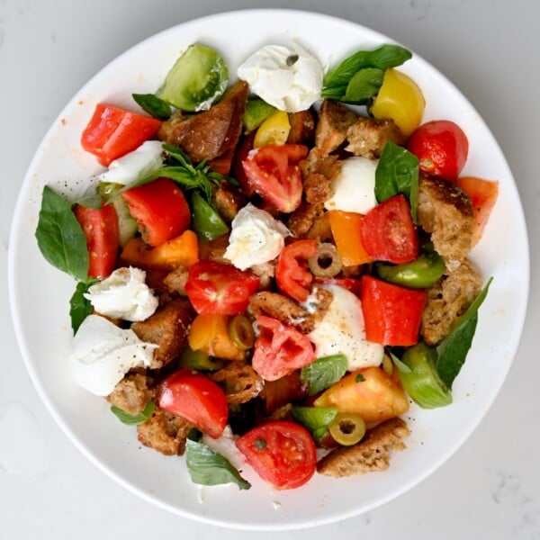 Top view of panzanella salad served in a large white plate on a white marble background.