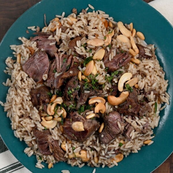A serving of mansaf with topping of cooked beef chunks, cashew nuts and parsley.