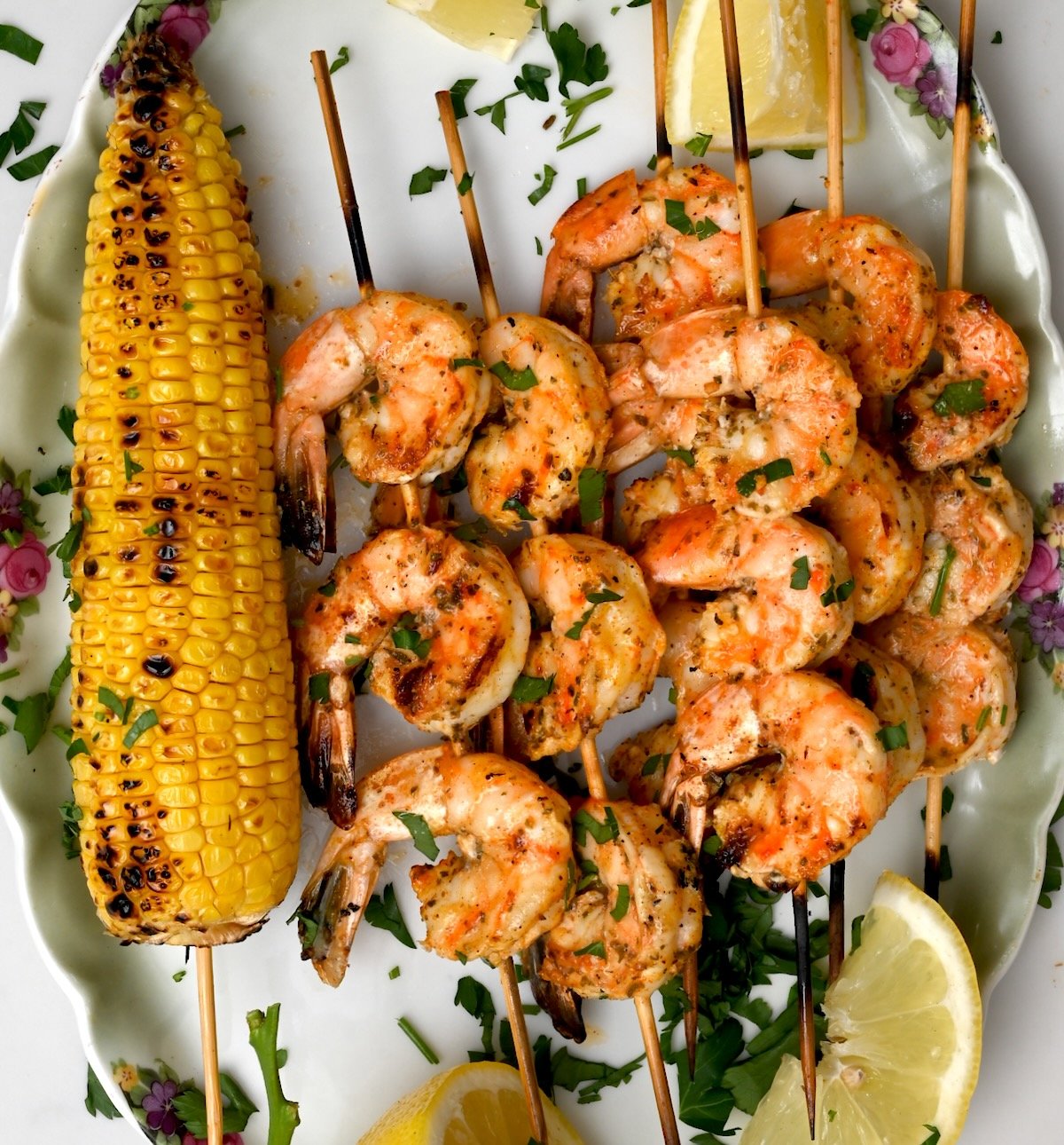 Shrimp skewers plated with lemon wedges and grilled corn