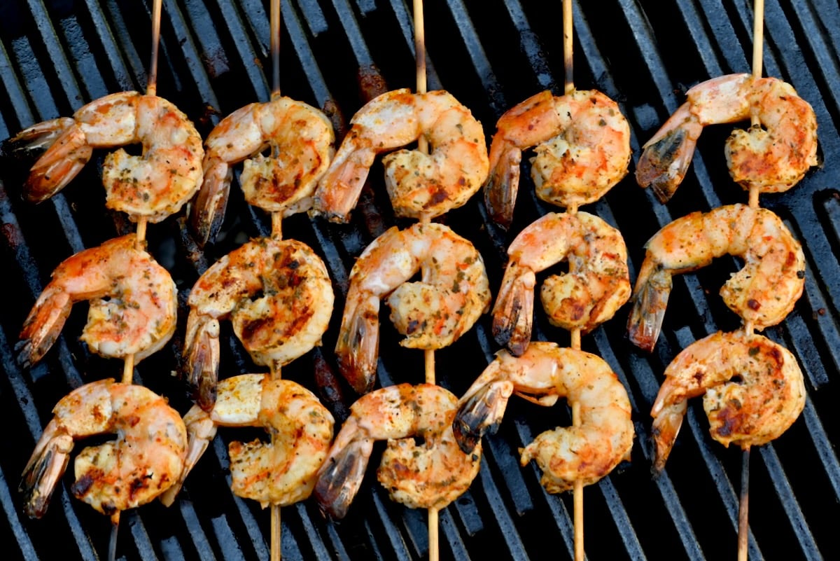 Side view of grilled shrimp skewers – five wooden skewers with cooked shrimp on a black grill grate.