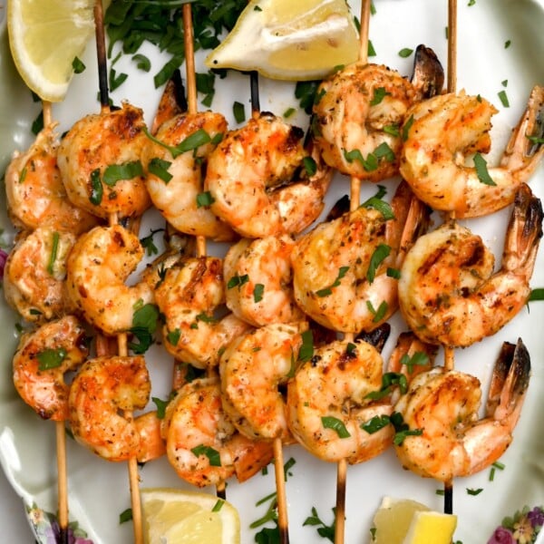 Shrimp skewers plated with garnish – Square top view of shrimp skewers on a green plate with parsley and lemon wedges.