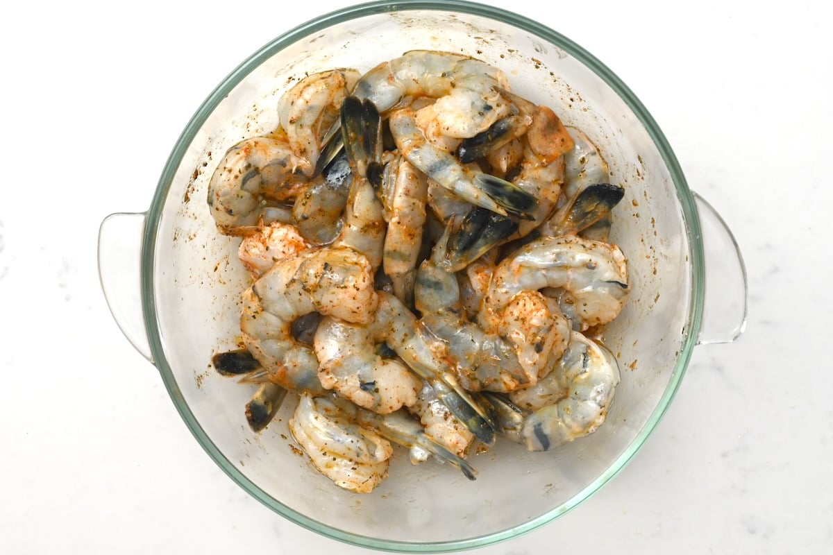 Marinated shrimp in bowl – Top view of raw jumbo shrimp coated in marinade inside a glass bowl on white marble.