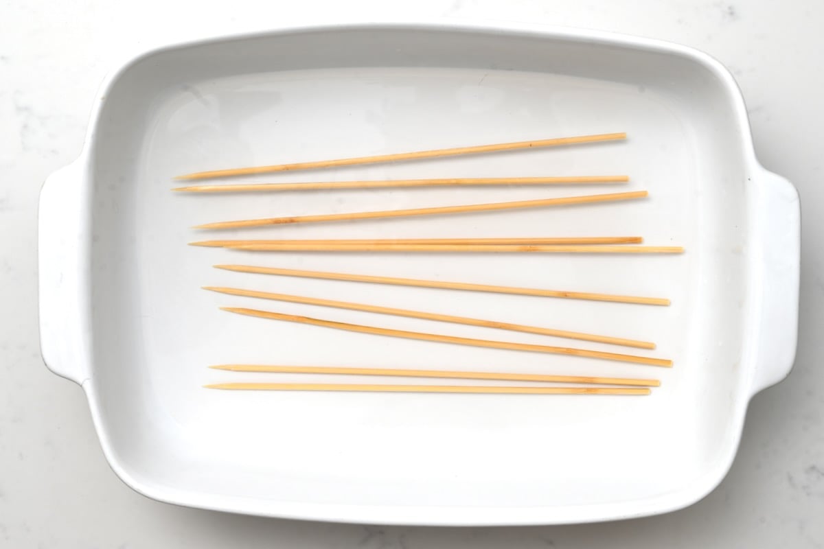 Soaking skewers in water – Top view of wooden skewers soaking in a large white 9x12 container.