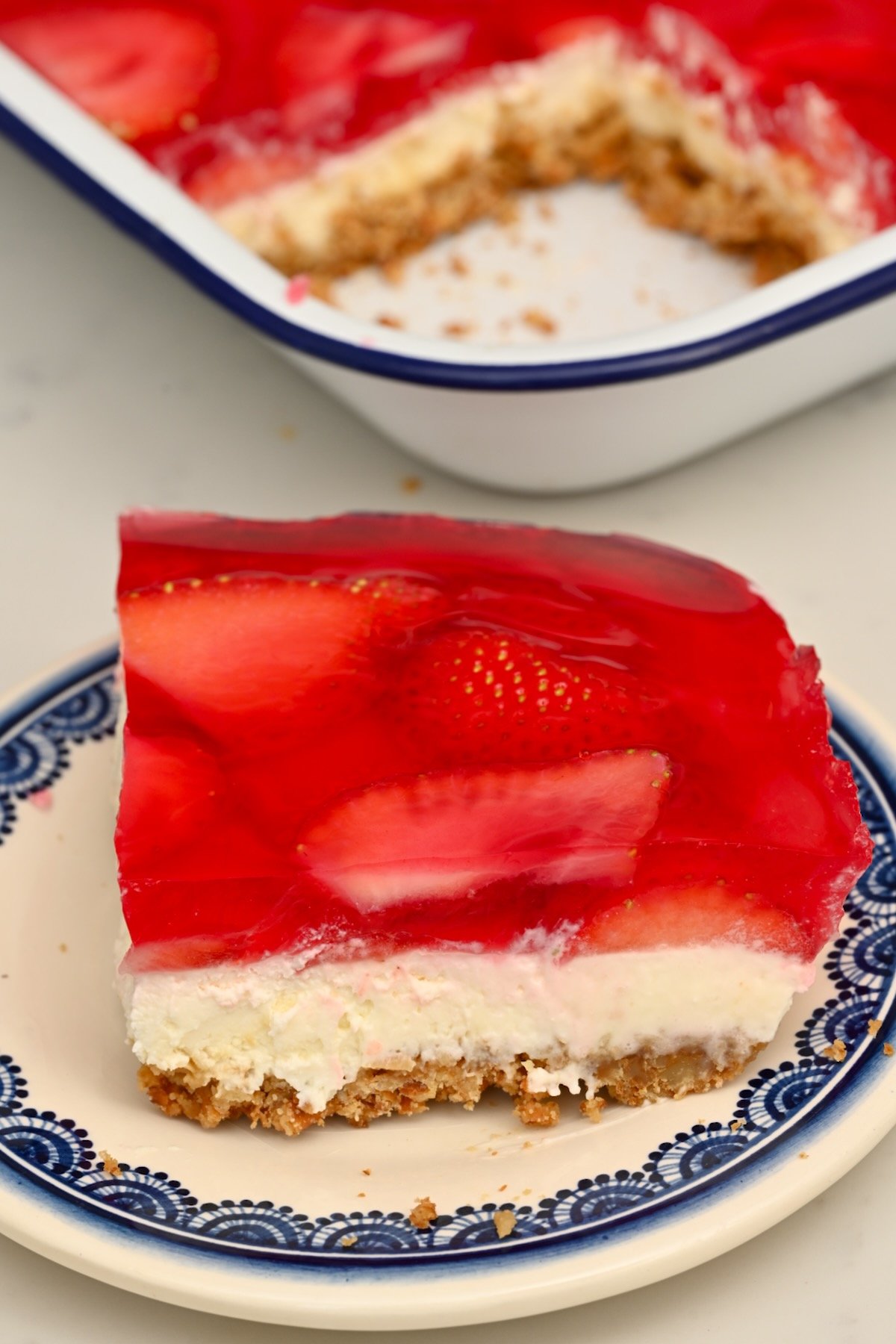 Side angle of a plated Strawberry Pretzel Salad slice with the full tray in the background. - 1