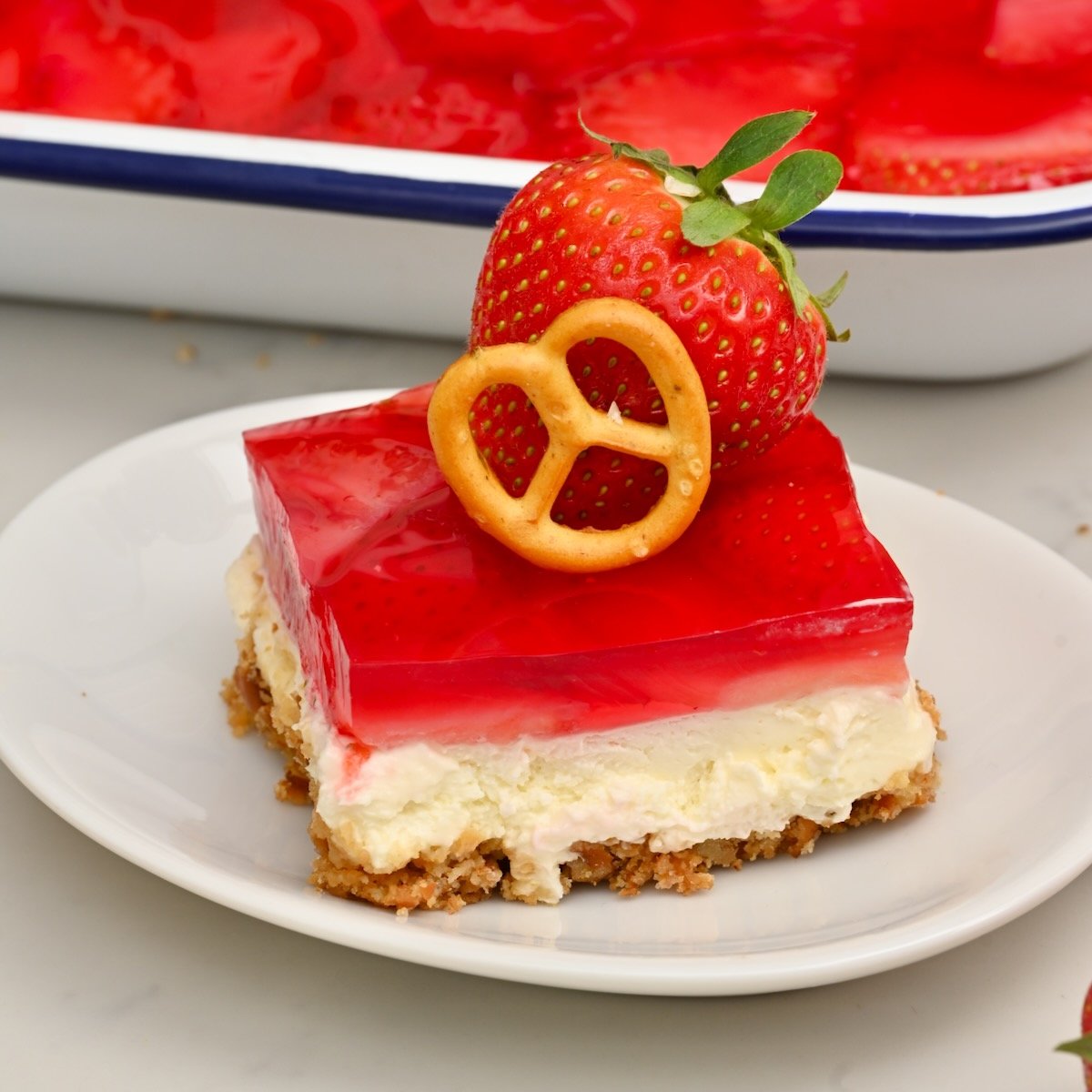 Slice of Strawberry Pretzel Salad with all three layers, topped with a small pretzel and a fresh strawberry. - 7