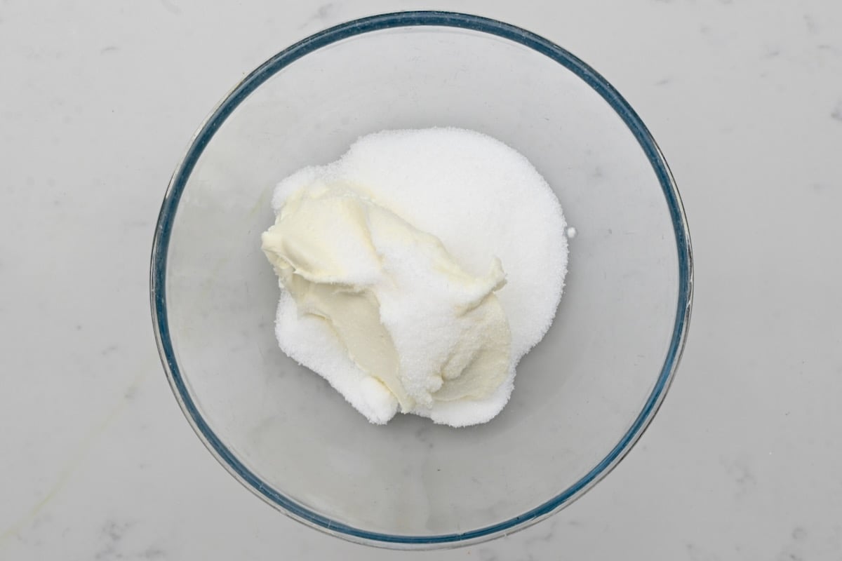 Unmixed cream cheese and sugar in a glass bowl on white marble. - 4