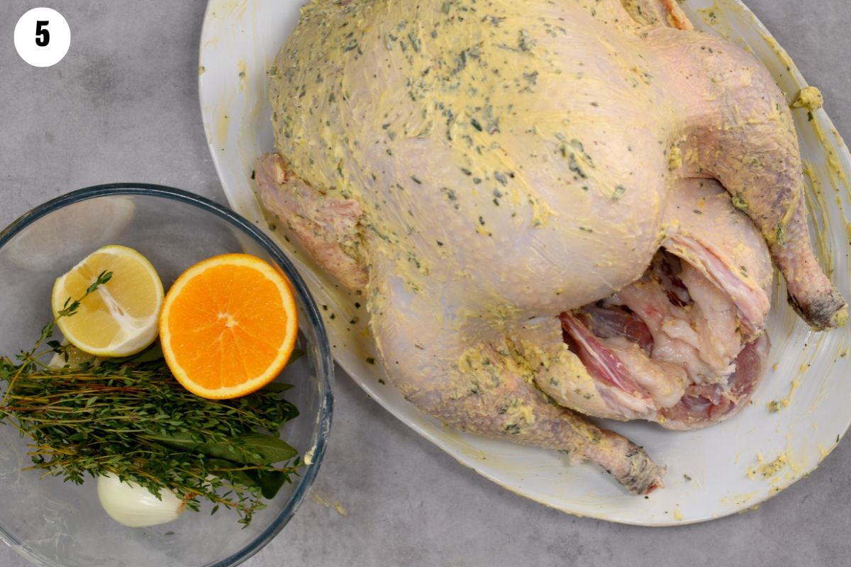Photo of a turkey fully coated with herb butter, with fresh vegetables and herbs beside it for stuffing the cavity. - 8