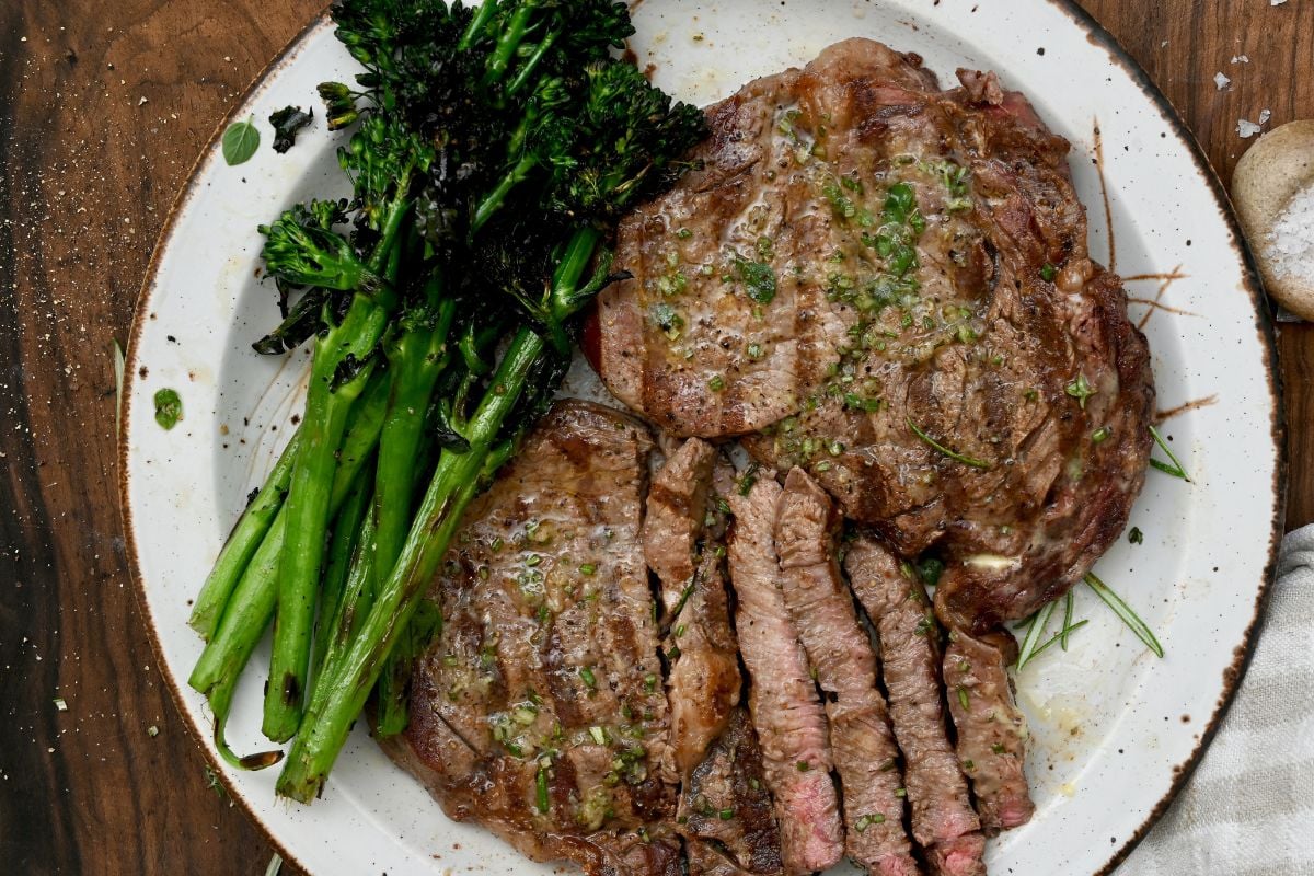 Grilled broccolini served alongside steak on a white plate. - 7