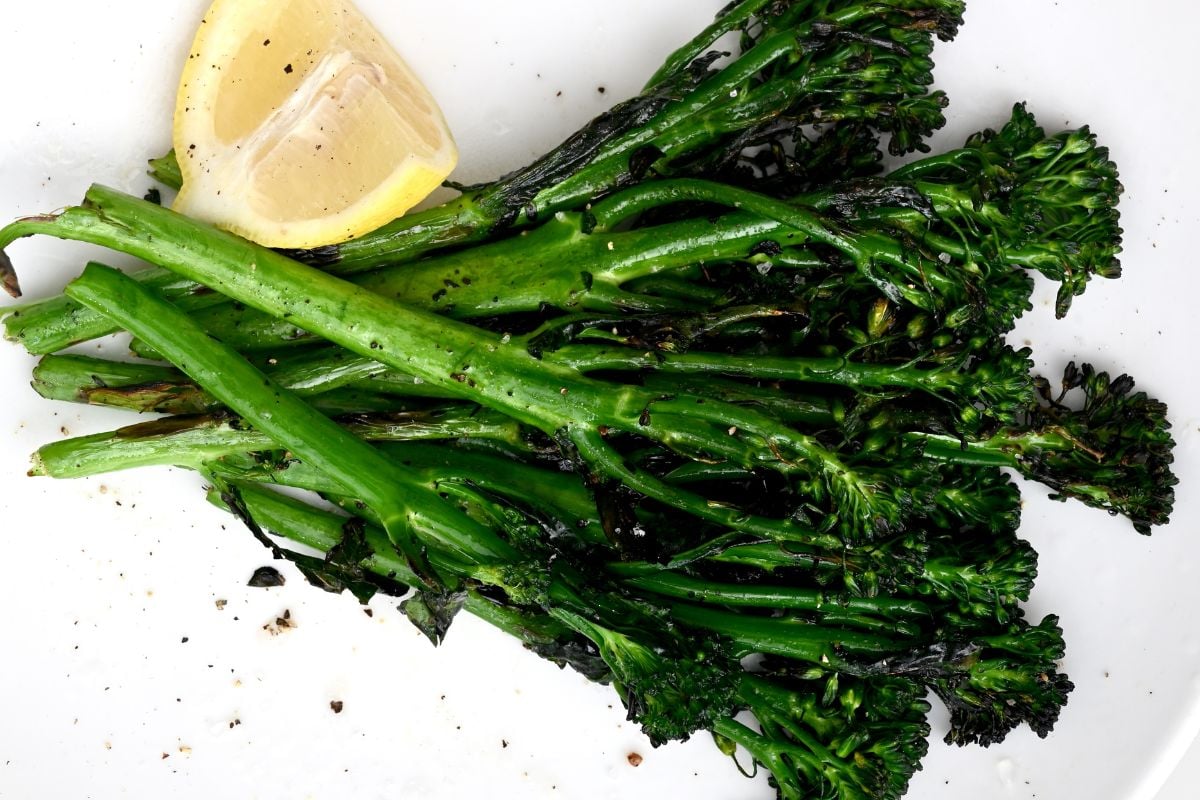 Grilled broccolini served on a white plate with a lemon wedge on the side. - 6