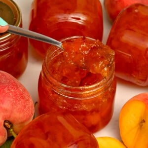 Side view of peach jam in a spoon with peaches and jars on the side - 10