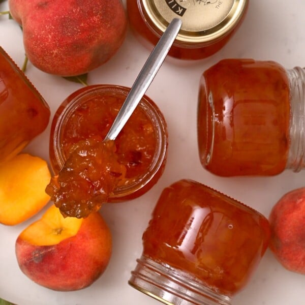 top view of peach jam in a spoon with peaches and jars on the side