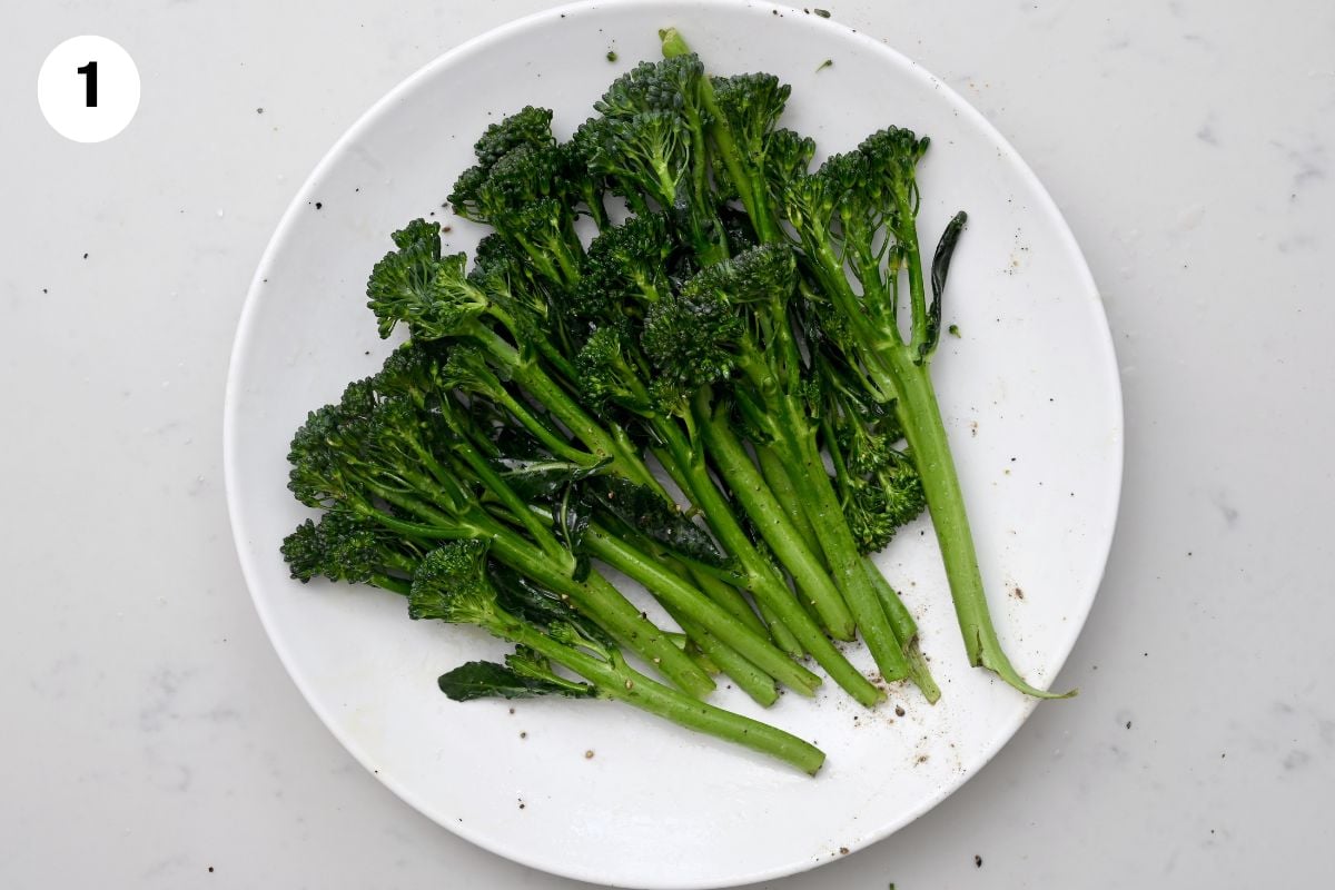 Broccolini being tossed with oil, salt, and pepper in a bowl, ready for grilling. - 3