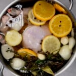 top view of turkey submerged in brine with herbs and veggies in a large metal pot. - 7
