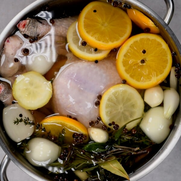 top view of turkey submerged in brine with herbs and veggies in a large metal pot.