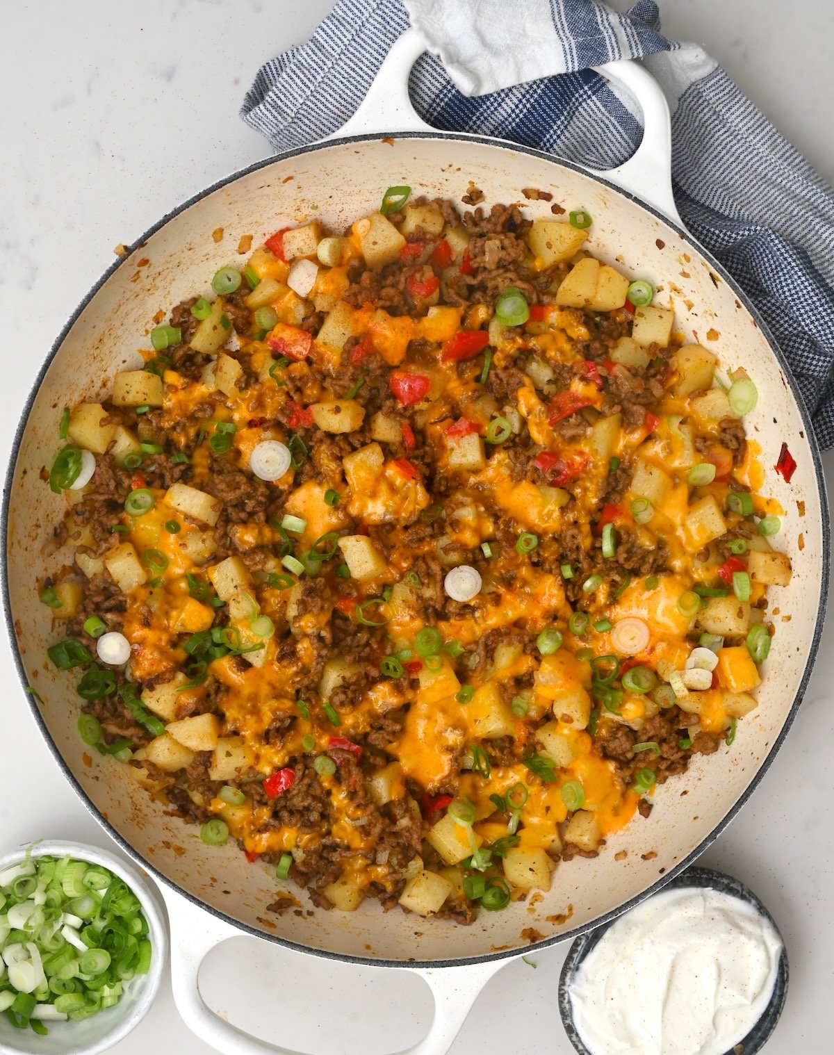 top view of ground beef and potatoes in a large white skillet with sour cream and green onions on the side - 1