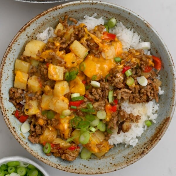 top view of ground beef and potatoes on top of white rice in a green bowl with chopped green onions