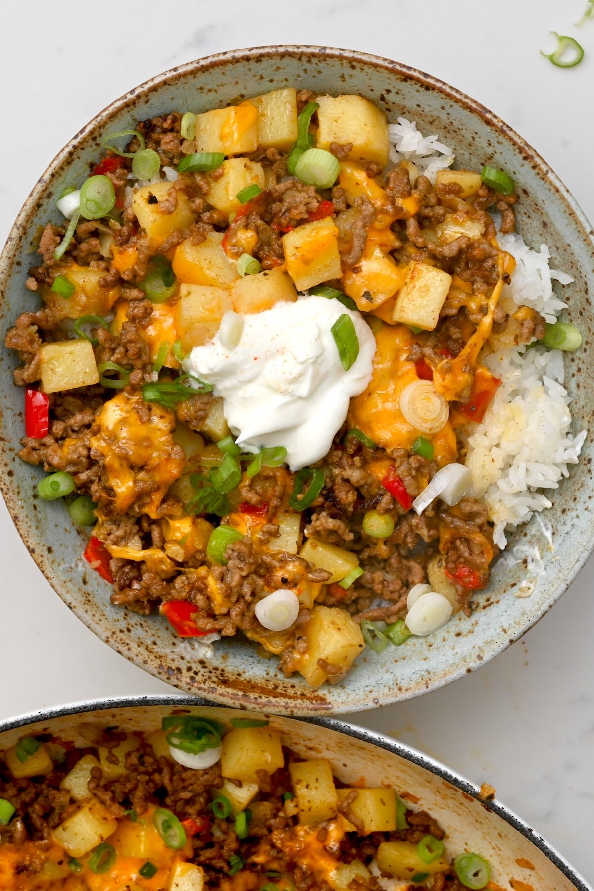 top view of ground beef and potatoes on top of white rice in a green bowl with sour cream on top - 2