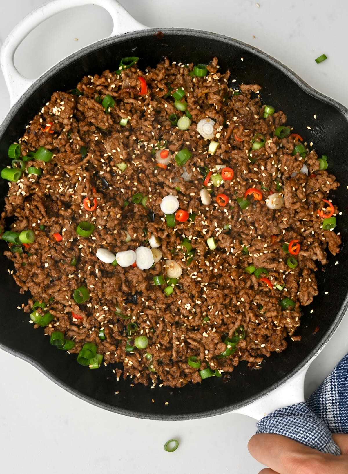 top view of black skillet with korean minced beef garnished with green onions and fresh red chillies - 2