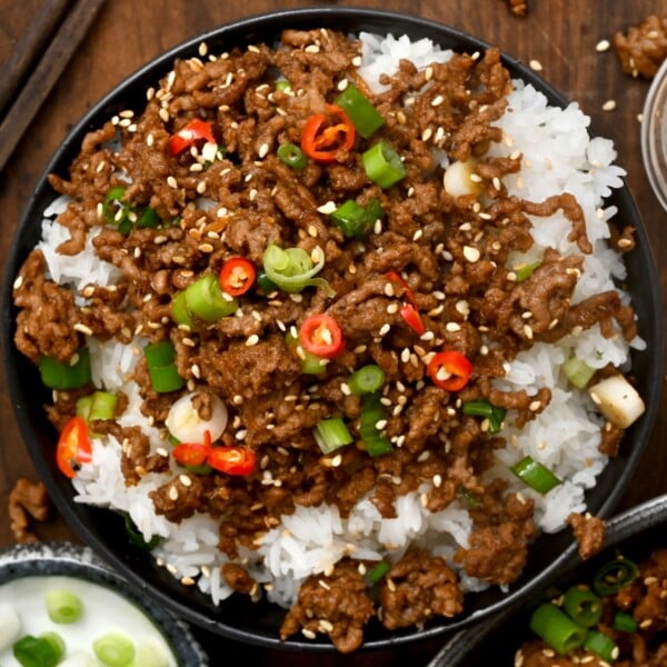 black bowl of korean minced beef on top of rice garnished with green onions and fresh red chillies