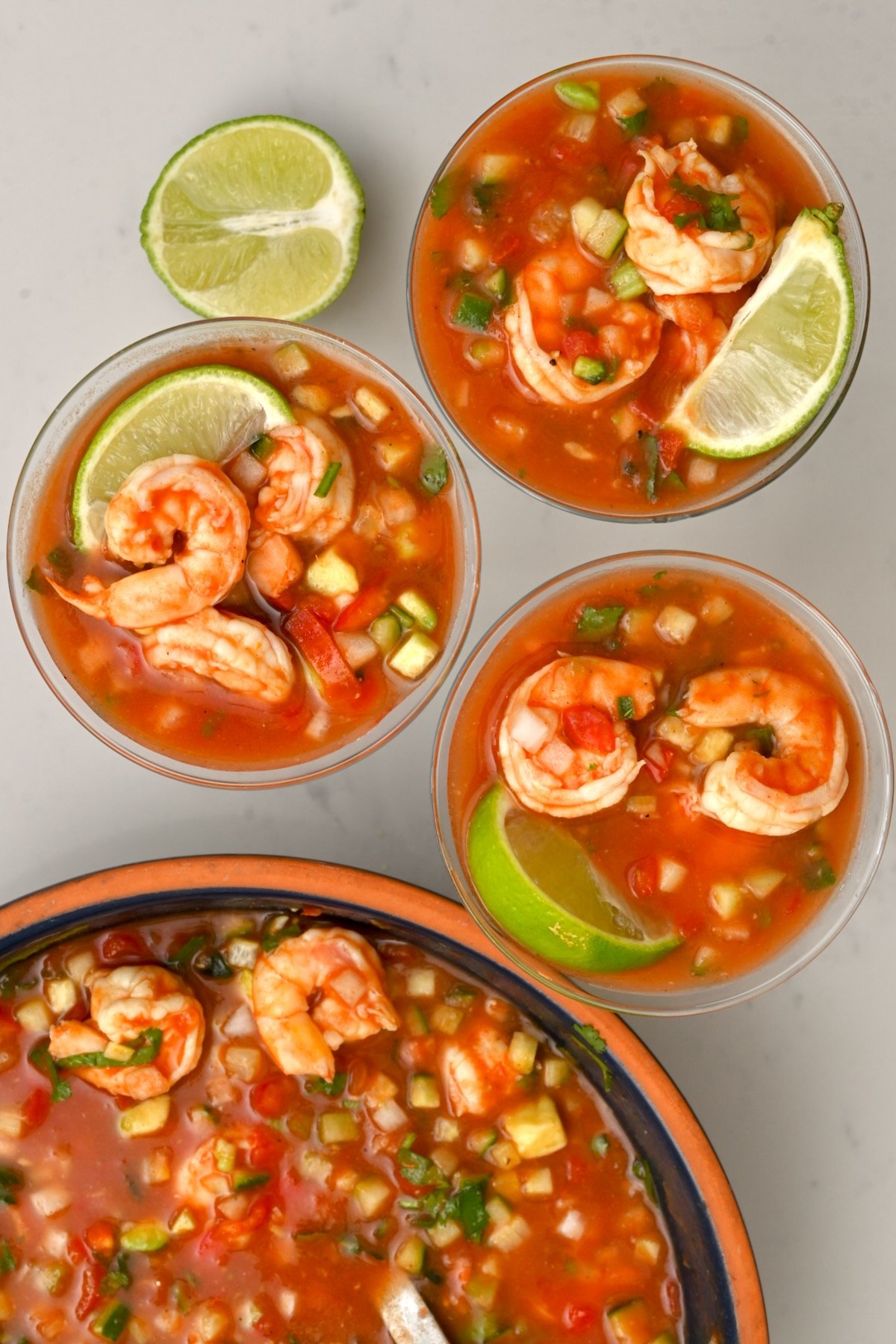 Top view of three mexican shrimp cocktail glasses with large bowl on the side and lime wedges