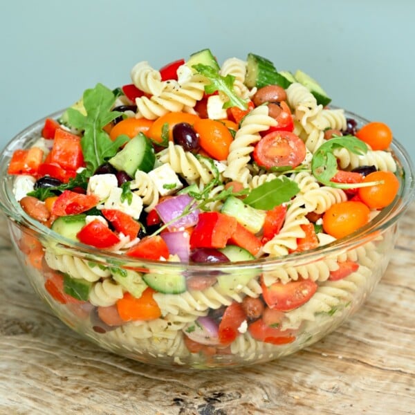 Side view of colorful pasta salad in a clear glass bowl filled.