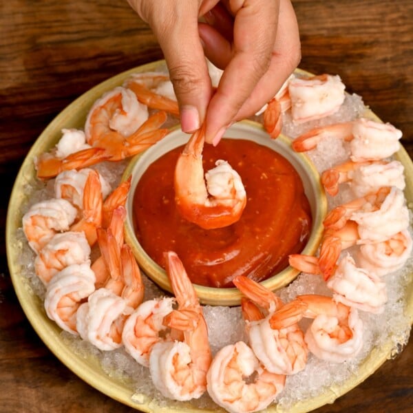 shrimp cocktail sauce surrounded by poached shrimp with hand holding one that is already dipped in sauce