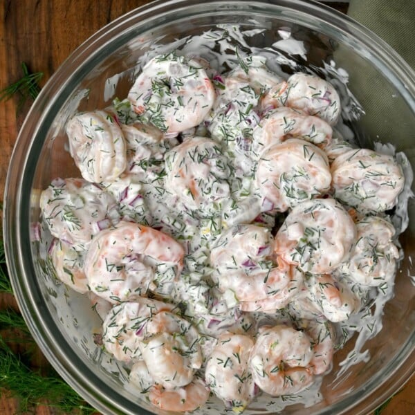 top view photo of a glass bowl filled with shrimp salad on top of wooden board