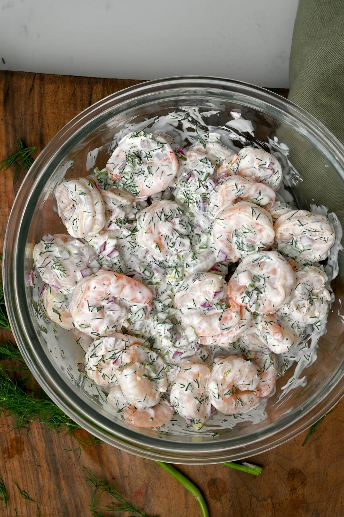 top view photo of a glass bowl filled with shrimp salad on top of wooden board - 1
