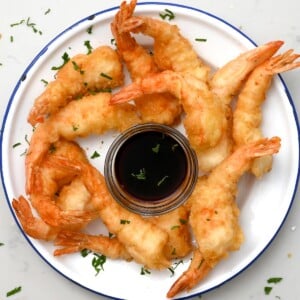 top view of shrimp tempura in a white plate with blue rip with dipping sauce in the middle