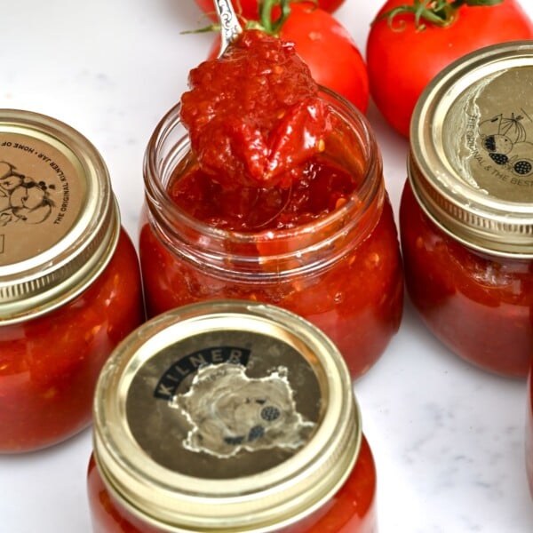 side view photo of tomato jam in a spoon with tomatoes in the background
