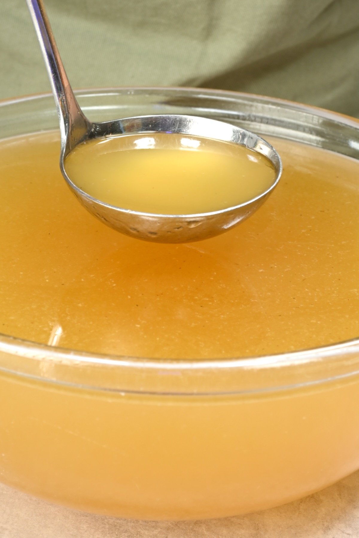 Ladle scooping golden turkey stock from a glass bowl. - 1